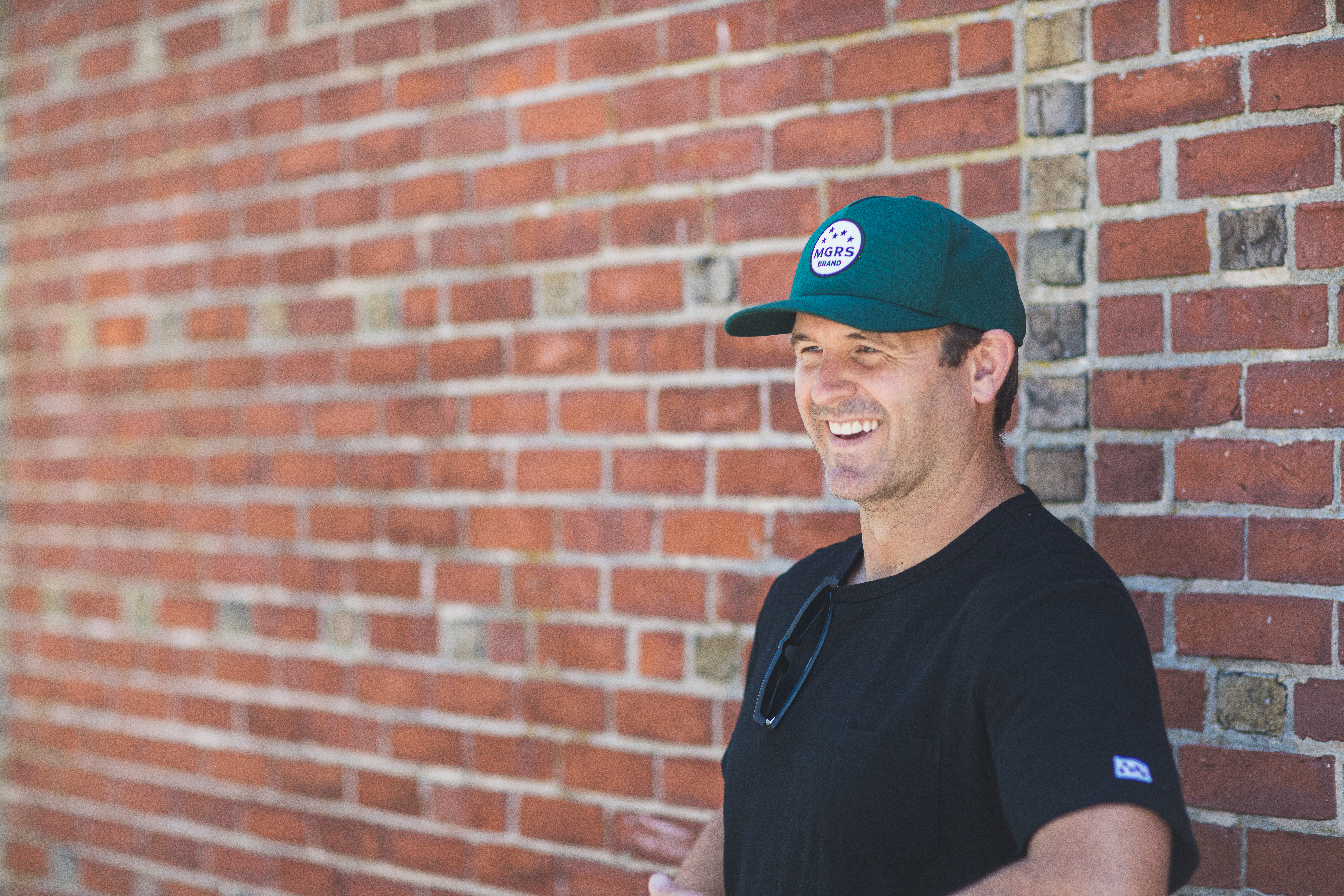 MGRS Brand founder Jamie Wallace stands in front of a brick wall wearing a green baseball hat