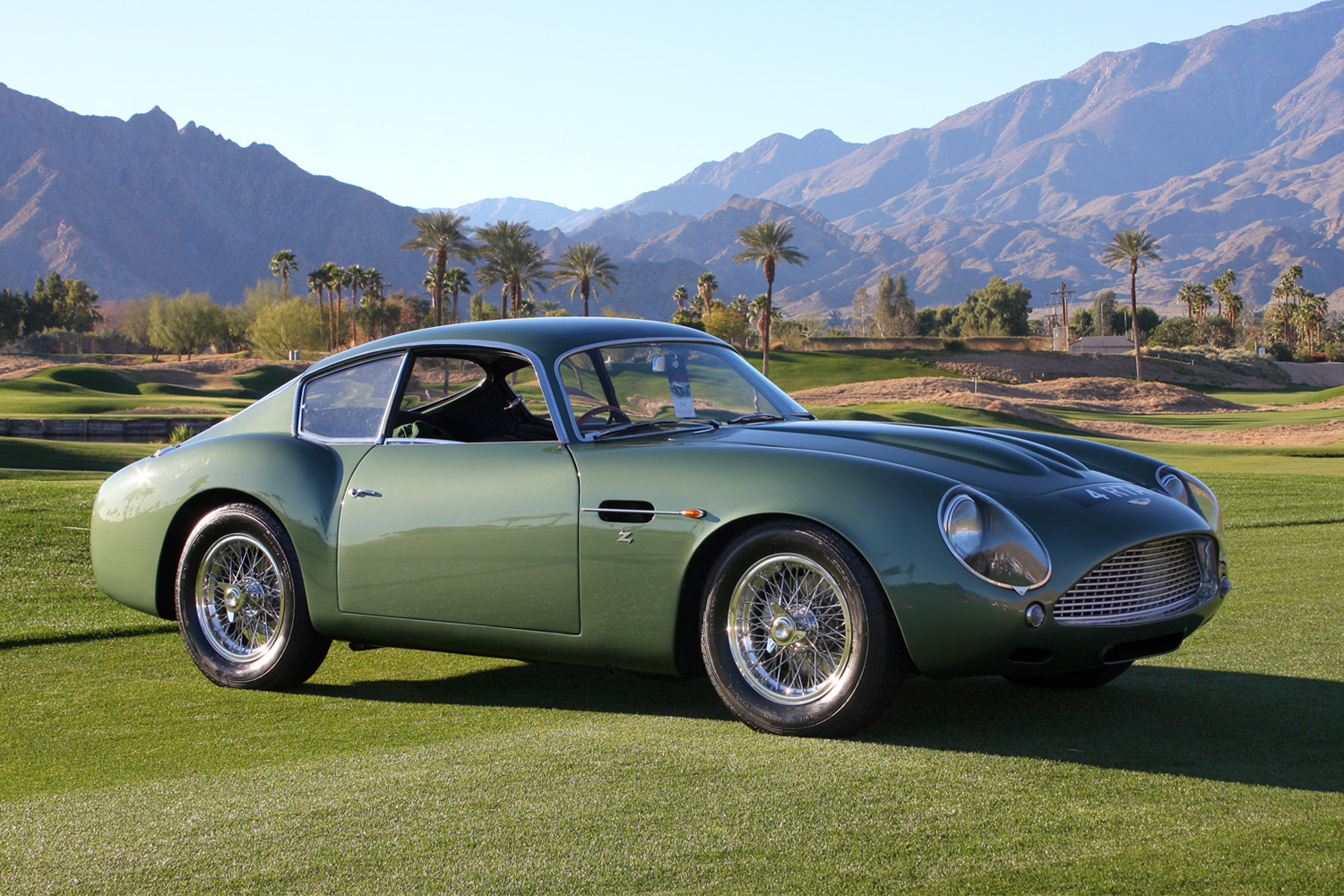 A green 1961 Aston Martin DB4 GT Zagato sports car sitting on a golf course with mountains in the background