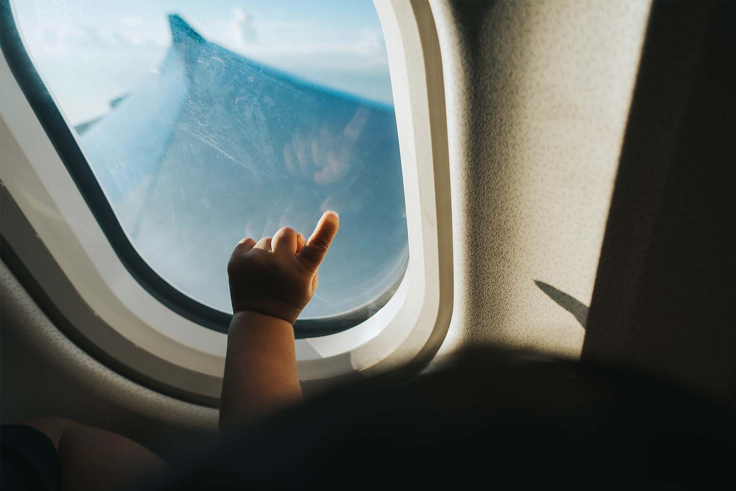 Hand of a toddler pointing airplane window against blue sky while traveling
