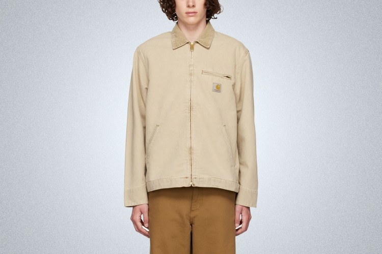 a model in a slightly cropped tan workwear jacket from Carhartt WIP on a grey background