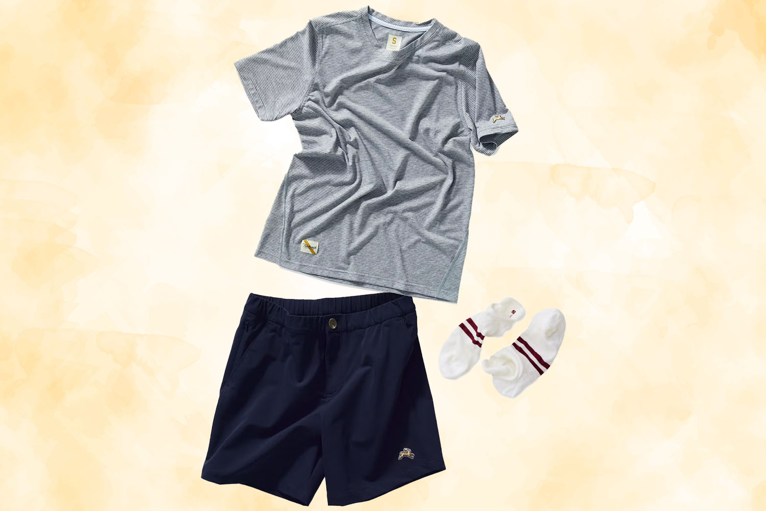 an Easy Going kit with a grey tee, navy shorts and socks from Tracksmith on a gold textured background