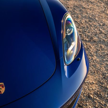 The hood and front left headlight of a blue Porsche Boxster. Porsche is now expected to launch an IPO in September 2022.