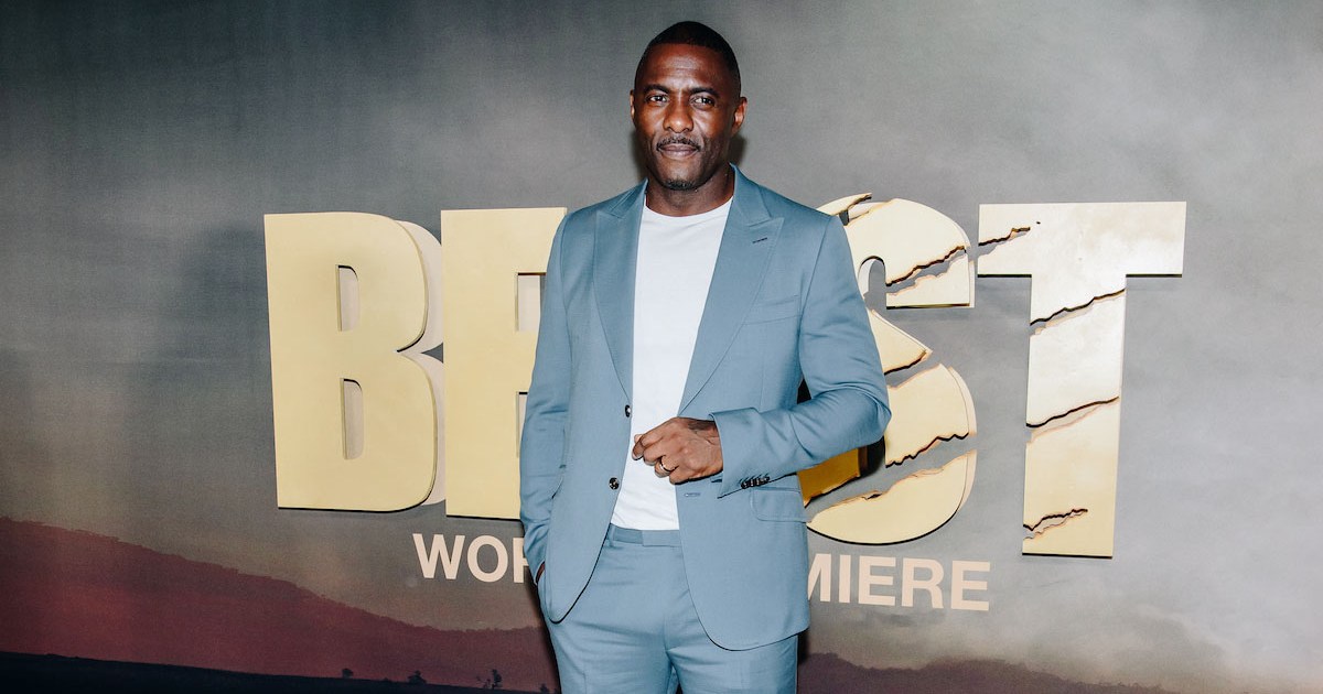 A photograph of actor Idris Elba at the Premier of "Beast" in a light chambray bule suit and white tee shirt