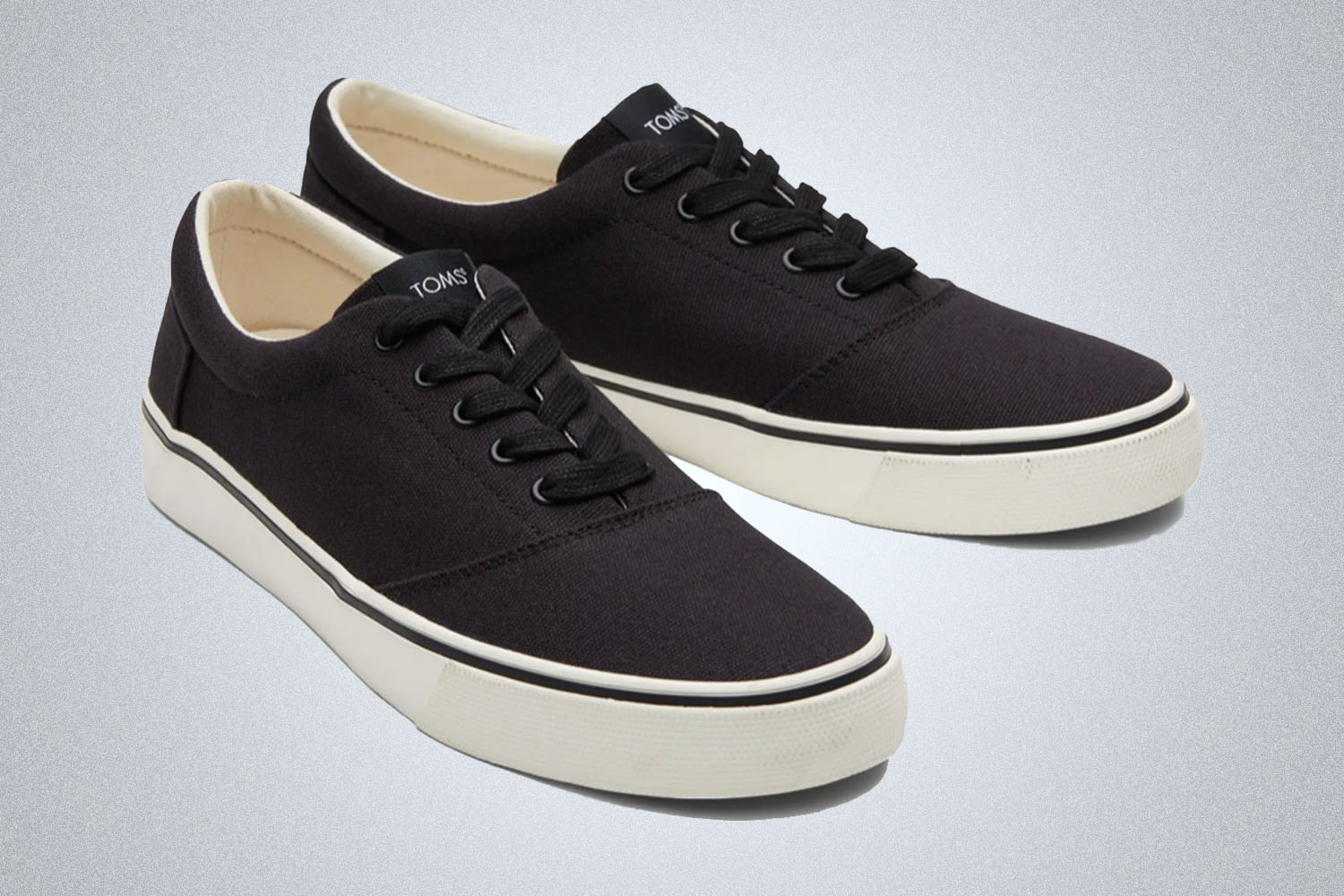 a pair of lightweight black sneakers from Toms on a grey background