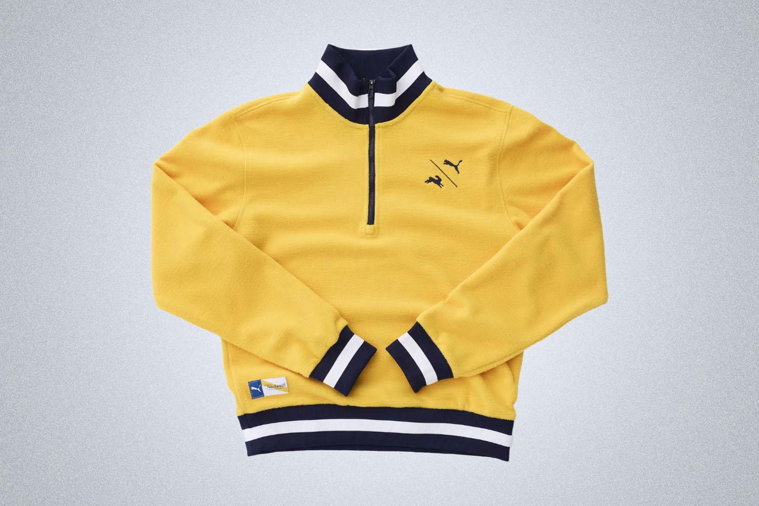 a yellow, blue and white quarter zip from Puma x Tracksmith on a grey background