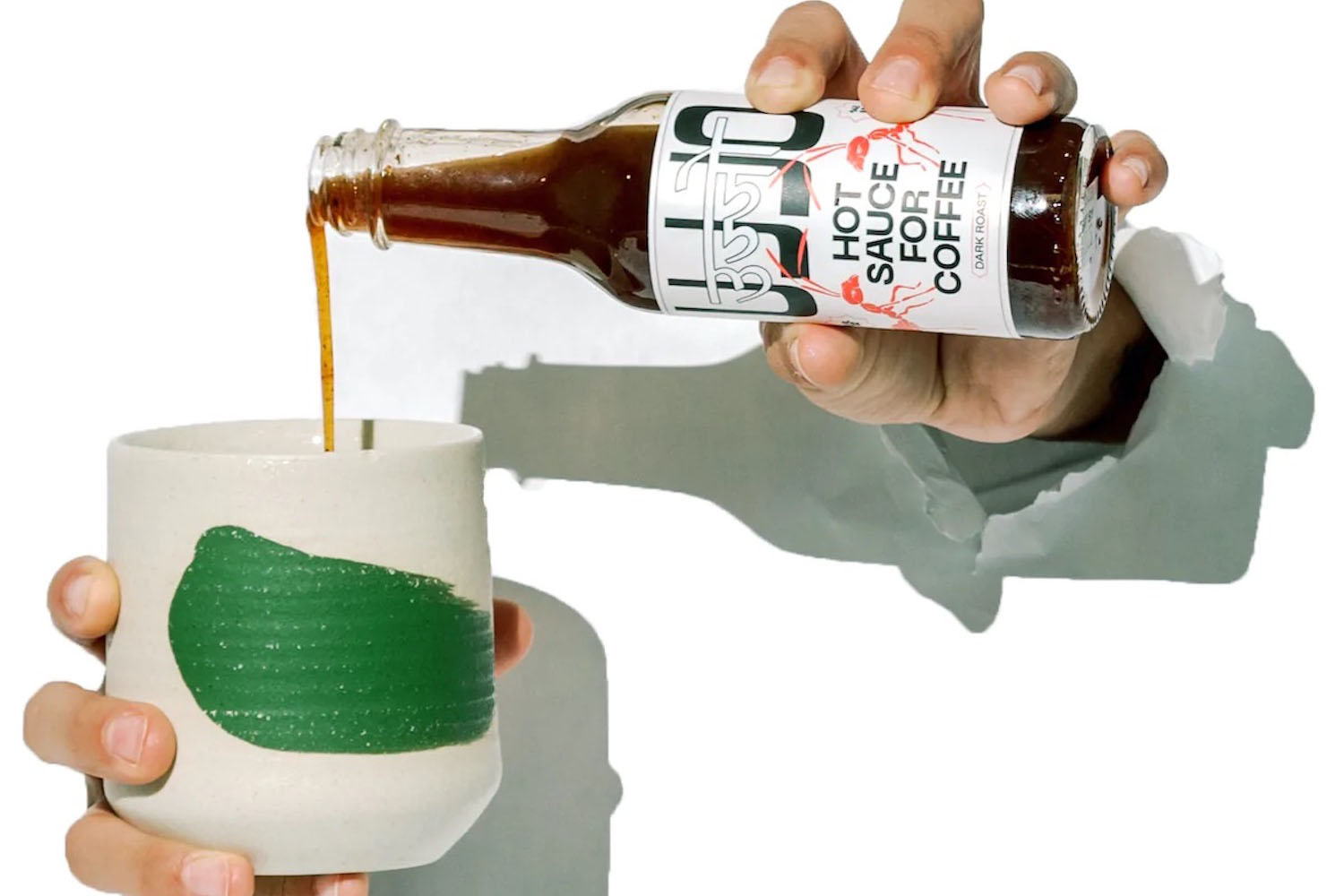 a hand pouring Uijo Coffee Hot Sauce into a cup on a white background