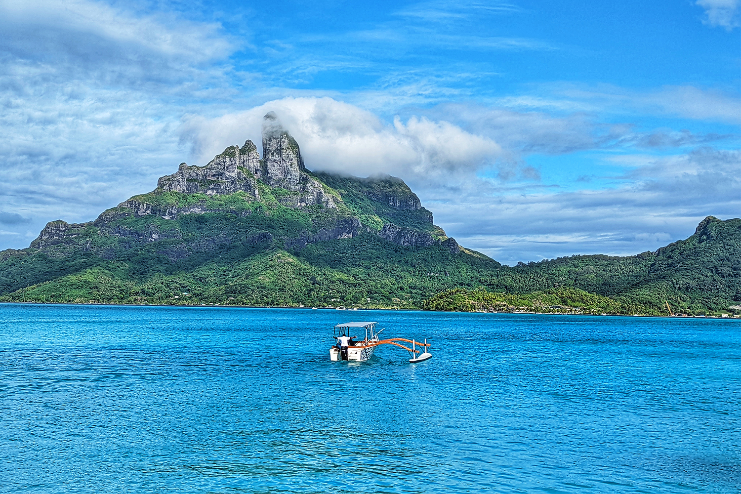 An outrigger boat in the ocean heading towards the island of Bora Bora in the Tahitian Islands of French Polynesia