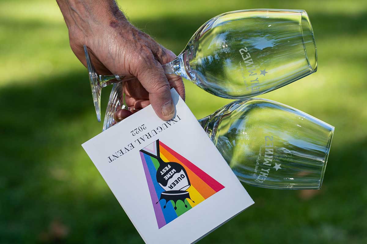 A program for Queer Wine Fest and two branded wine glasses