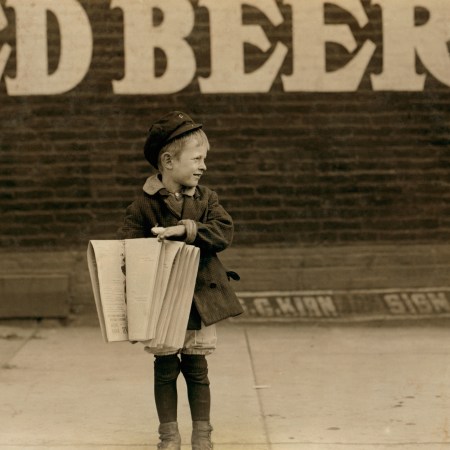 A newsie standing on a street corner in the early 20th century.