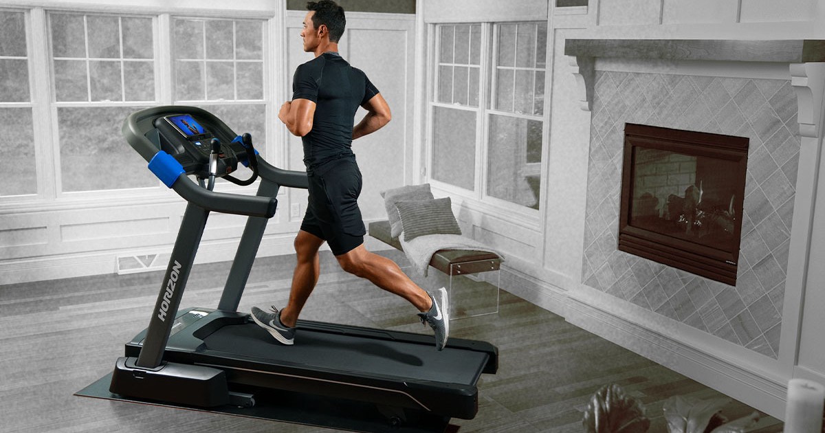 A man running on the Horizon Fitness 7.0 AT Studio Series Treadmill in a house