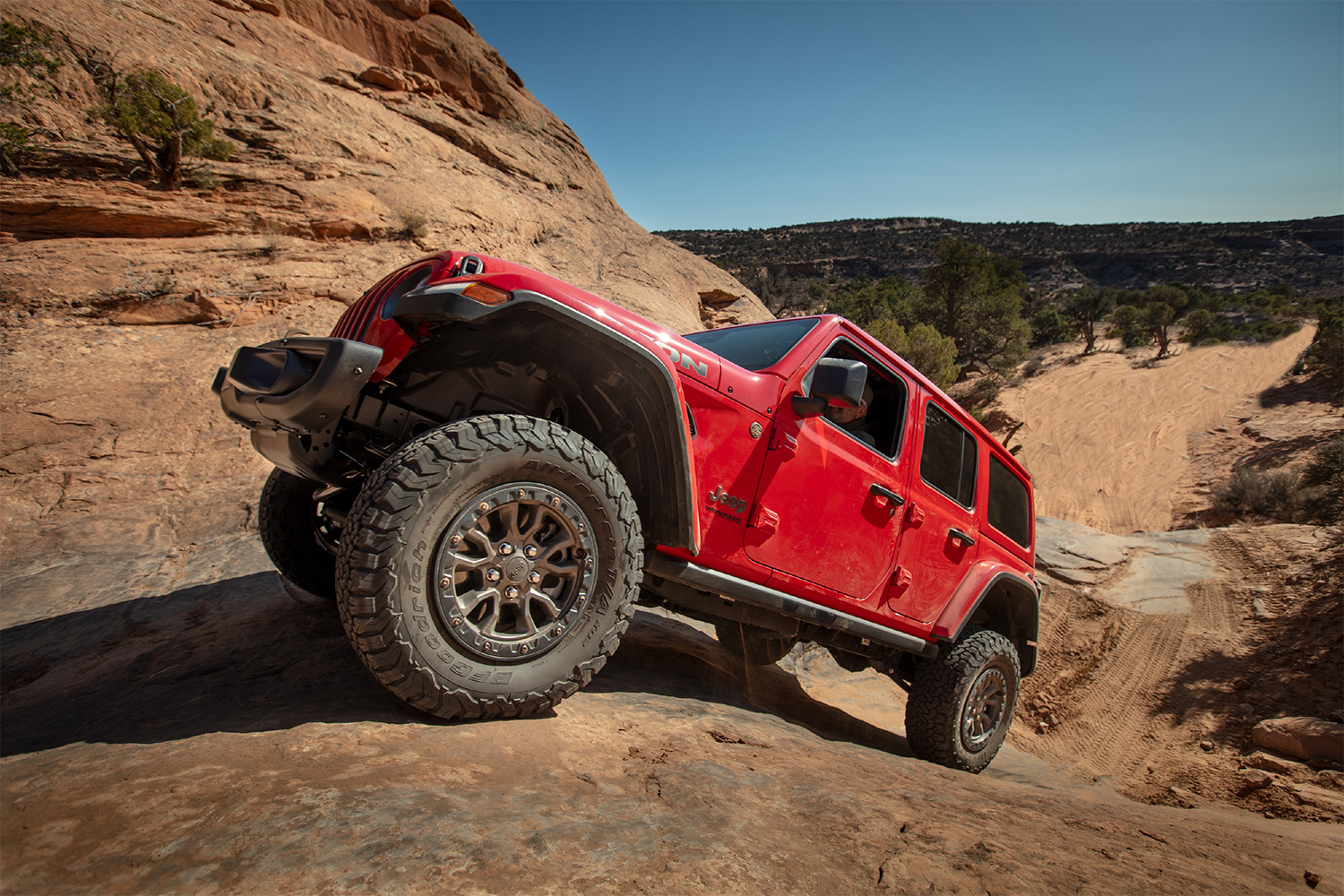 A red 2022 Jeep Wrangler Rubicon 392, a version of the SUV with a V8 engine, climbing up a rock face