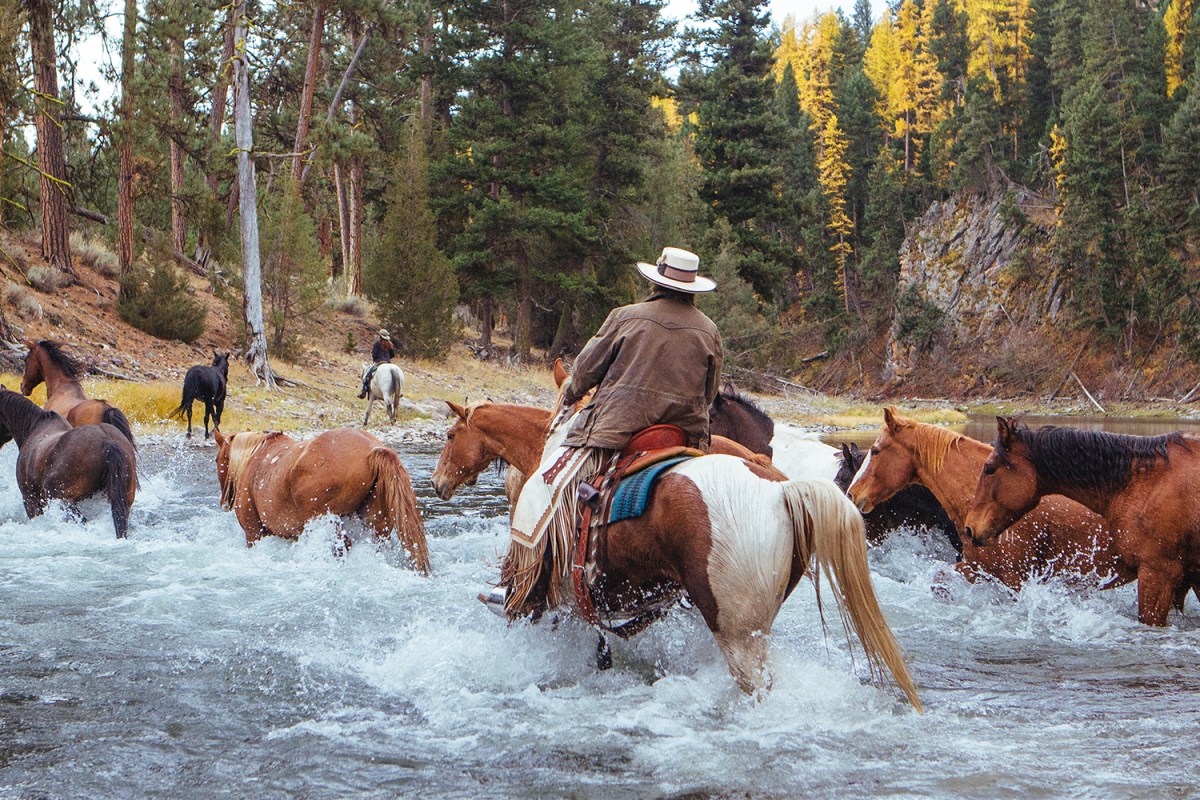 Horses and riders ford a river at Paws Up, a ranch in Montana, one of the best luxury ranches in the U.S.