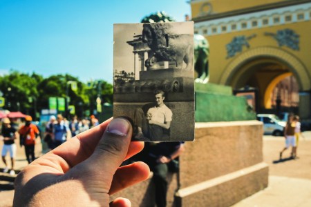 A man holding a photograph up in front of the same scene in present day.