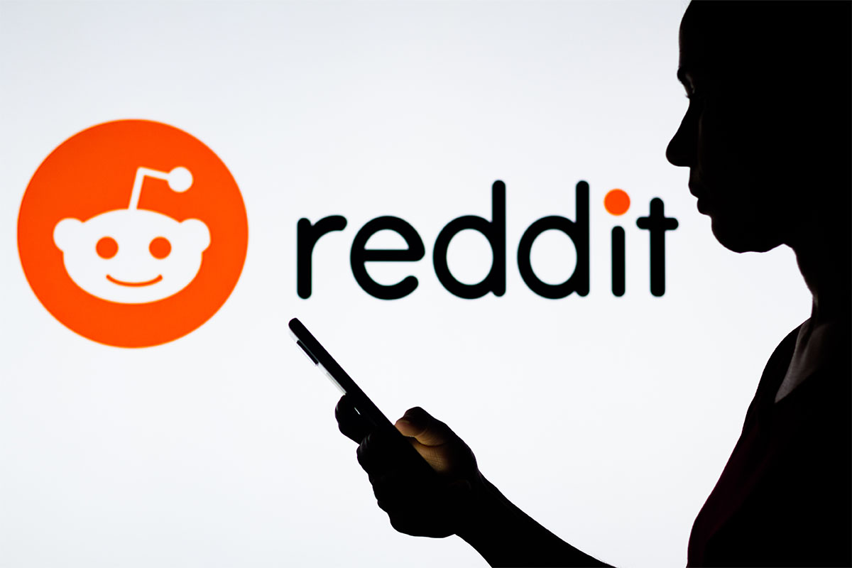 In this photo illustration, a woman's silhouette holds a smartphone with the Reddit logo in the background. A recently shutdown part of subreddit allowed users to trade and sell explicit photos of women without their consent