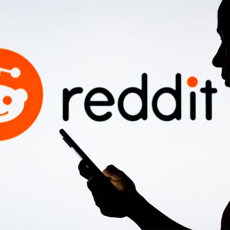 In this photo illustration, a woman's silhouette holds a smartphone with the Reddit logo in the background. A recently shutdown part of subreddit allowed users to trade and sell explicit photos of women without their consent