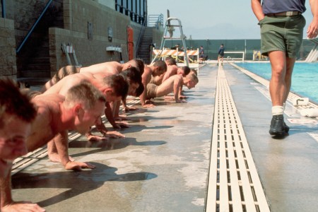 A group of Navy SEAL candidates performing push-ups next to a pool.