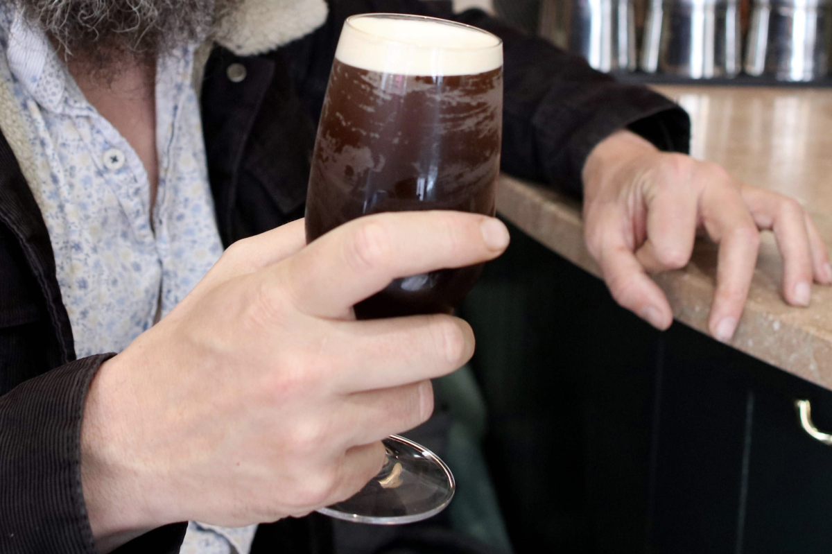 A man holding a frosty dark beer in a glass. Is this the summer of the tropical stout?