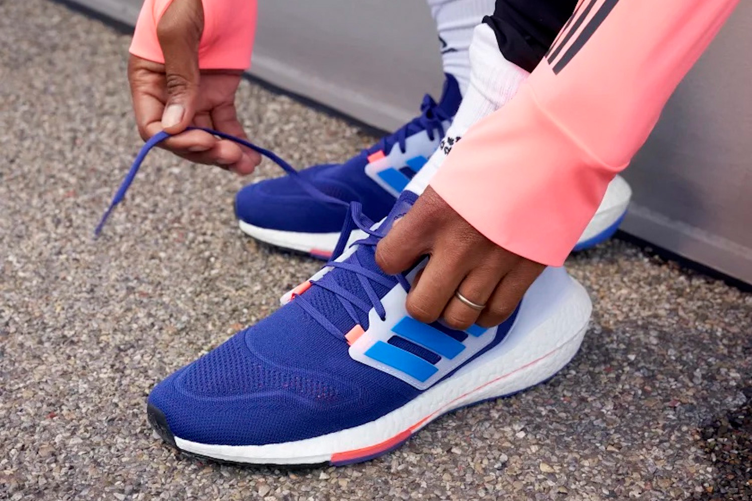 a model tying a pair of blue Adidas ultraboost 22 running shoes on pavement