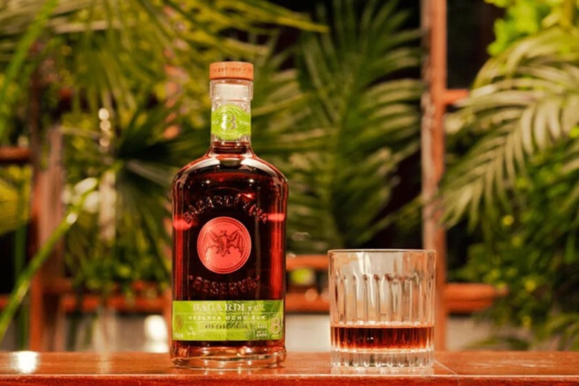 a bottle of Bacardi rum next to a poured glass on a wooden table against a green background