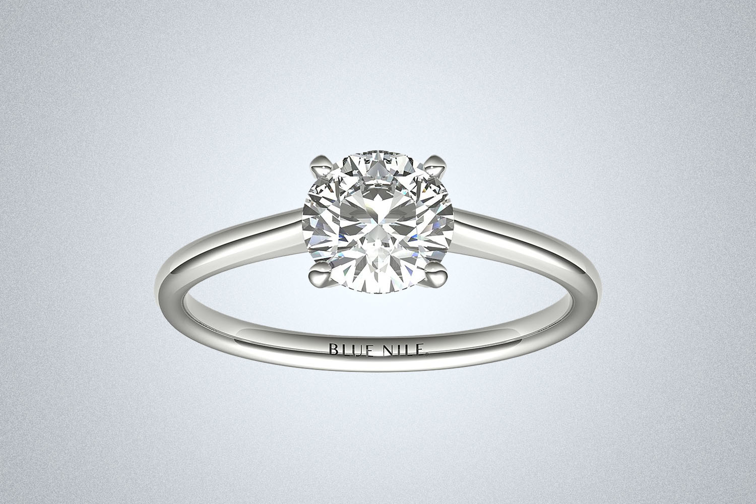 A Blue Nile Petite Solitaire Engagement Ring on a gray background