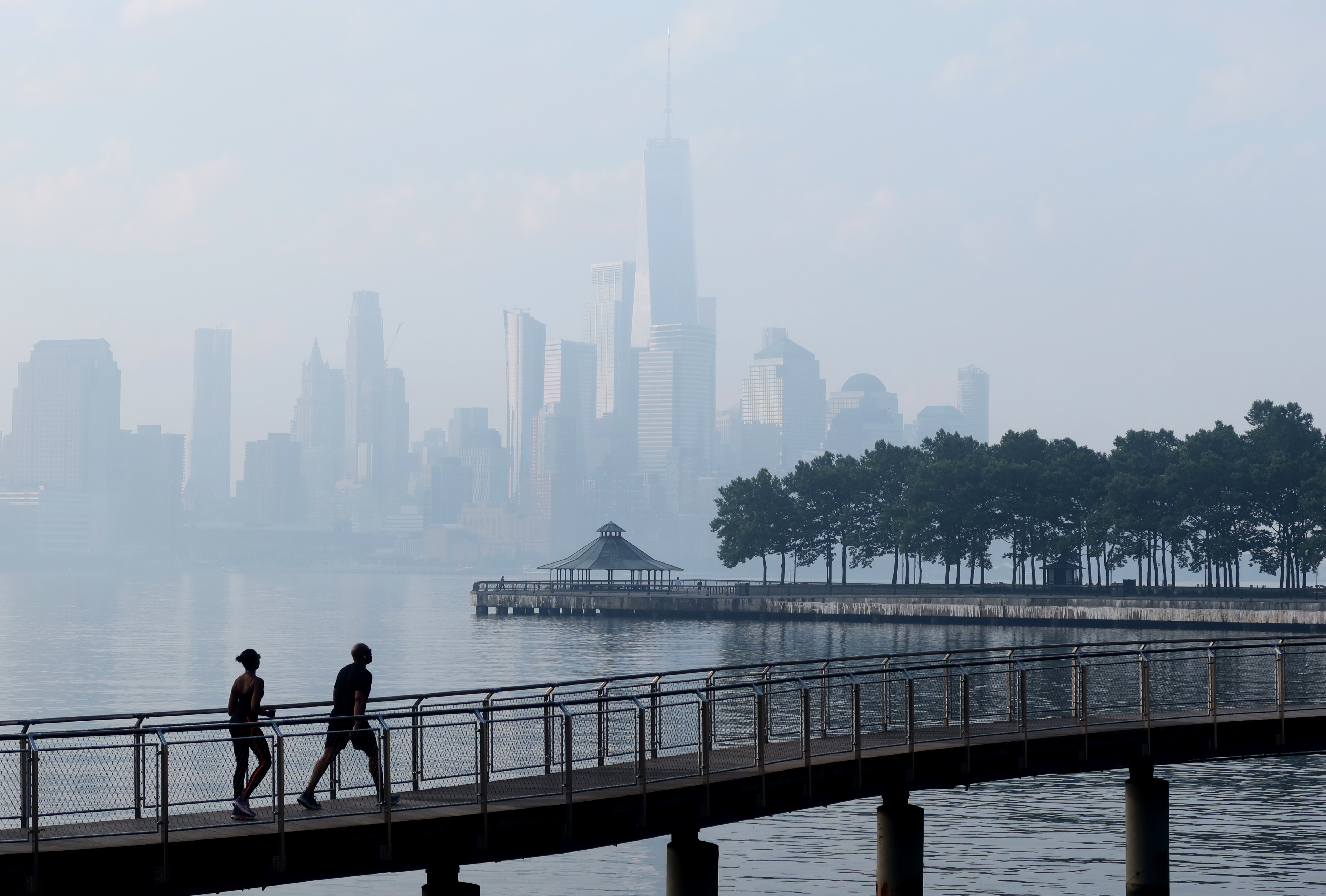 A couple walks on a boardwalk in Hoboken with Freedom Tower in the background.