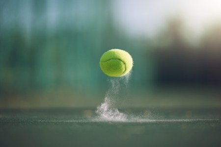 A closeup of a tennis ball bouncing off a clay surface.