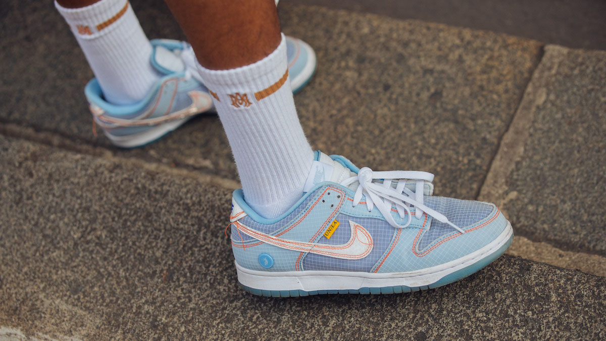 A photograph of a modle wearing blue and white Union LA x Nike Dunks on a stone road.