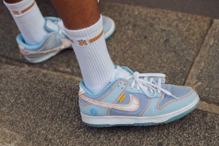 A photograph of a modle wearing blue and white Union LA x Nike Dunks on a stone road.