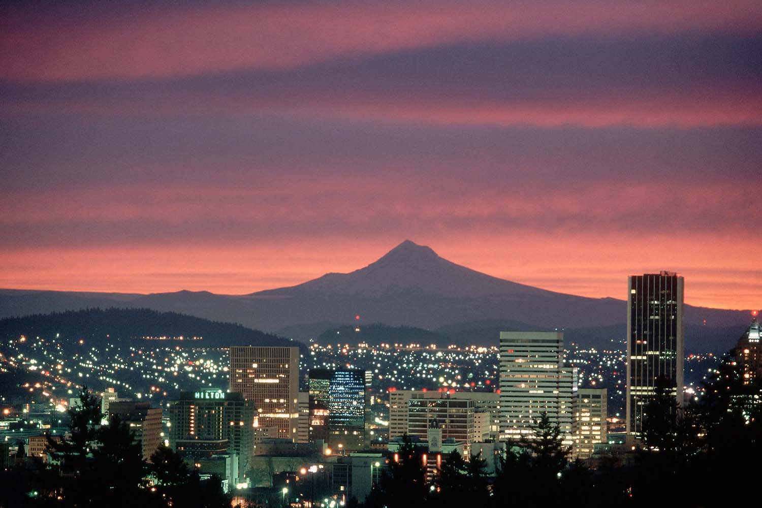 The sunrise casts a pink glow over the city of Portland and Mount Hood.