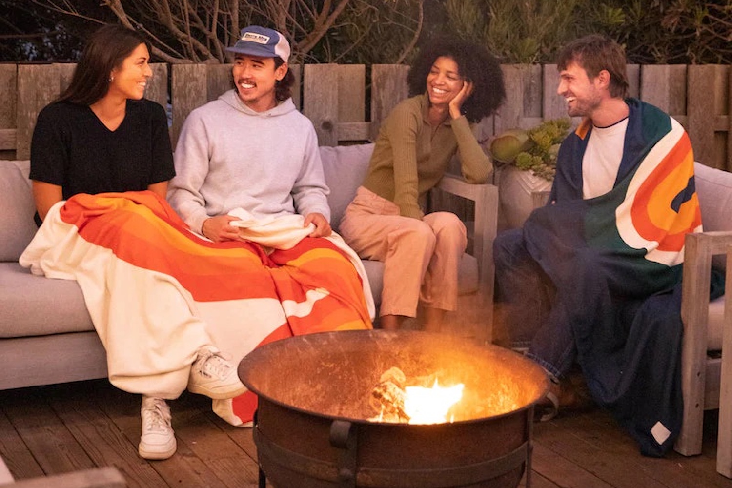 a quadruplet of people sitting on a couch in front of a fire drapped in RUMPL blankets