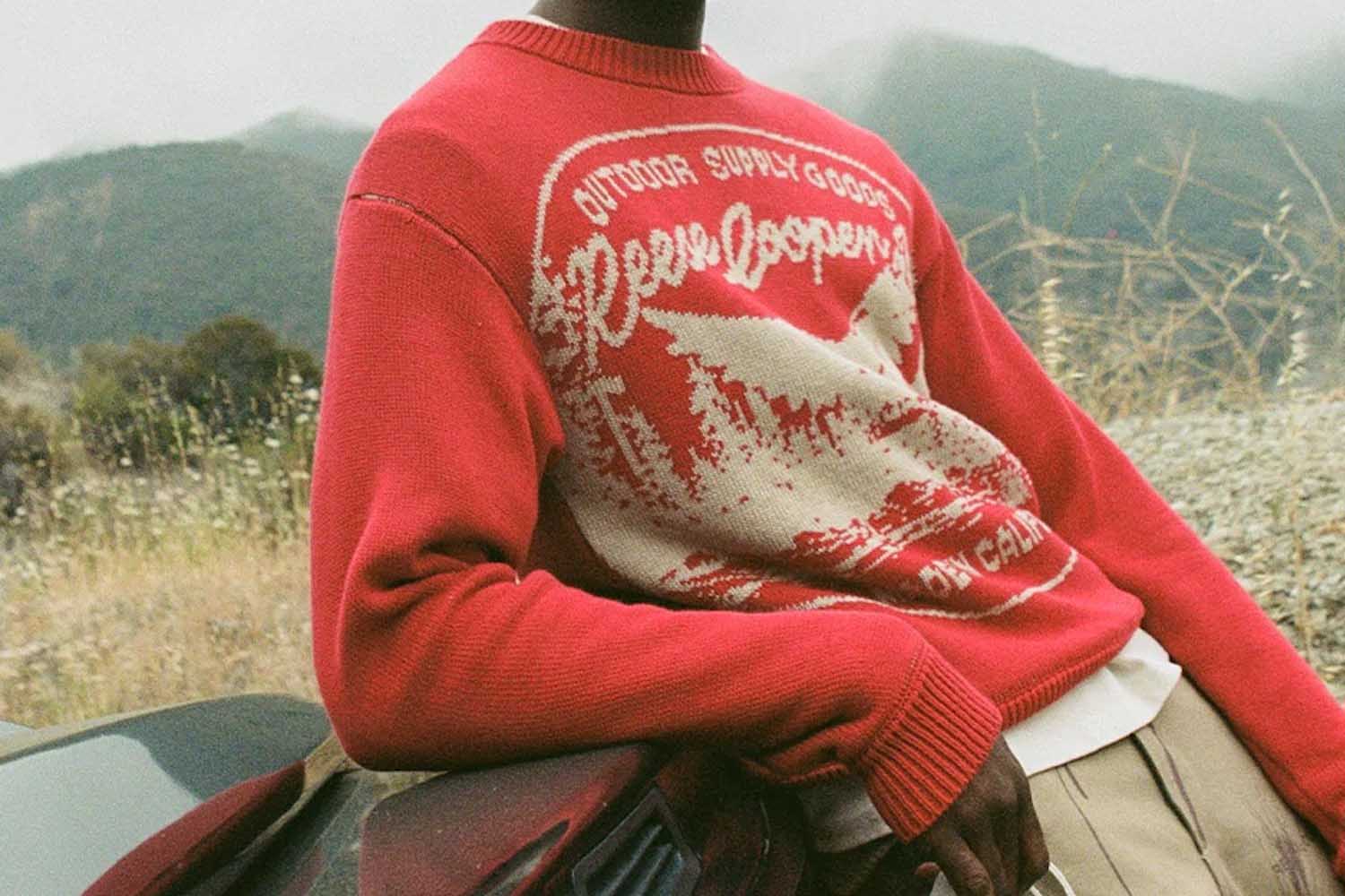 A model in a red knit Reese Cooper sweater against an outdoor backdrop