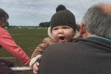 A baby yawning into the shoulder of an old man.
