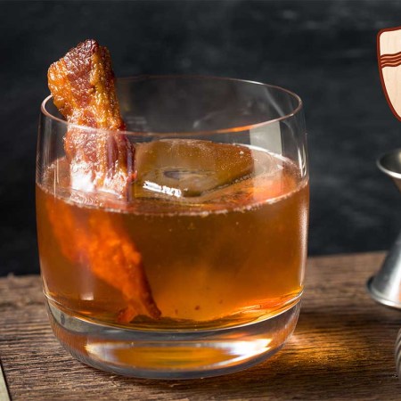 A bacon cocktail: a whiskey drink with bacon near a jigger and other mixing utensils. Bacon can be used in a cocktail in more ways than a garnish.