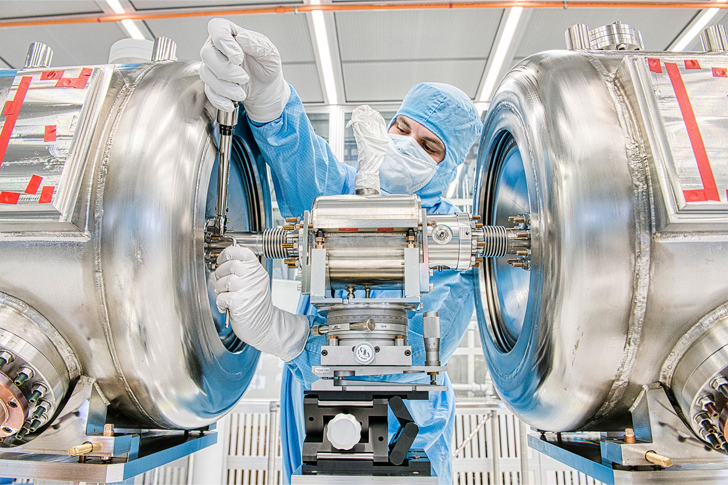 A technician in a clean room works on a spoke resonator of the PIP-II, an in-progress linear particle accelerator at Fermilab.