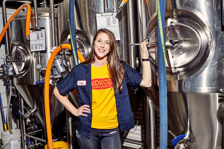Head brewer Katie Lowe of Koko's Bavarian standing next to their craft beer brewing equipment