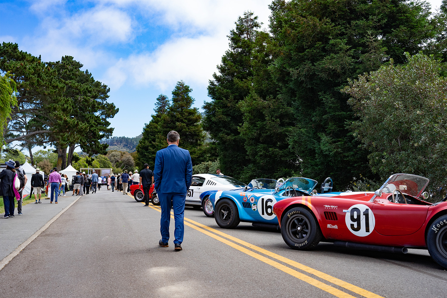 Man walks alongside cars on display at the Rolex Monterey Motorsports Reunion