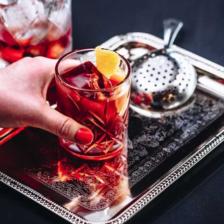 A Negroni in a rocks glass on a tray with a strainer and a mixing glass in the background. Negronis usually are made of equal parts