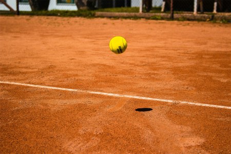A closeup of a tennis ball bouncing off a clay surface.