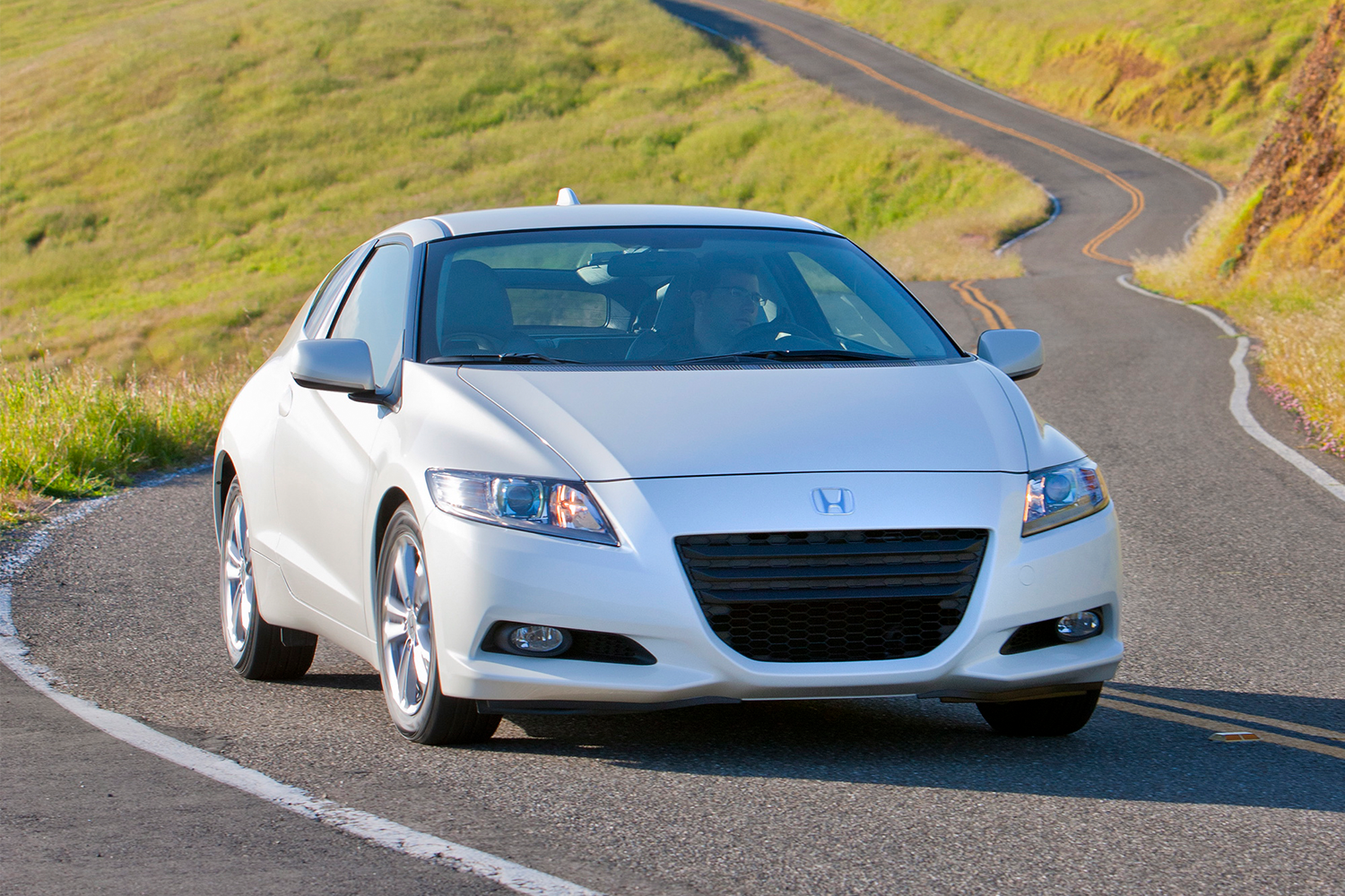 A white 2011 Honda CR-Z EX hybrid driving down a windy road in the countryside