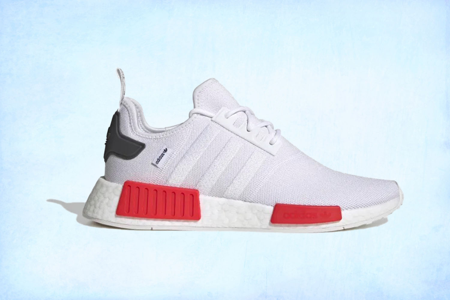 a pair of white Adidas NMD_R1 sneakers on a light blue background