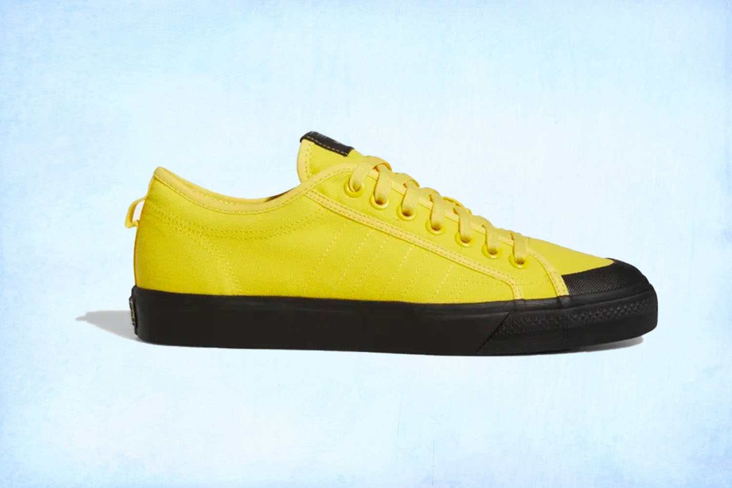 a pair of yellow Adidas Nizza sneakers on a light blue background