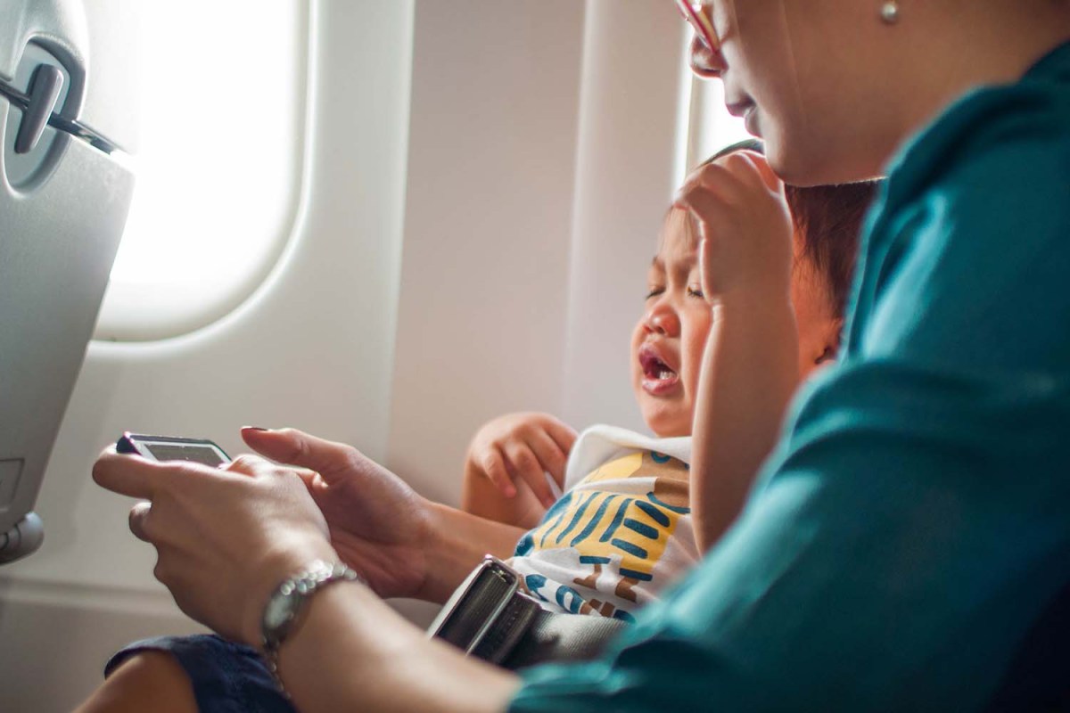 A mother and a crying baby watching a video in an airplane. Should babies be allowed on airplanes?