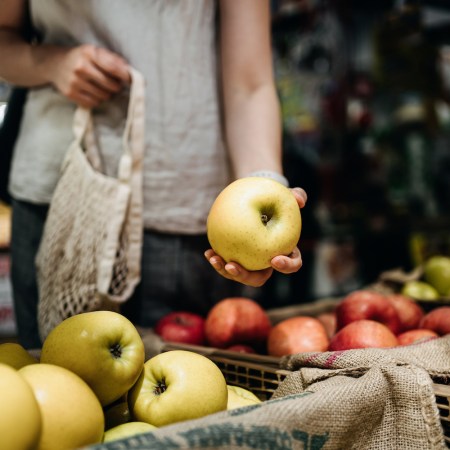 woman grocery shopping and holding a yellow apple