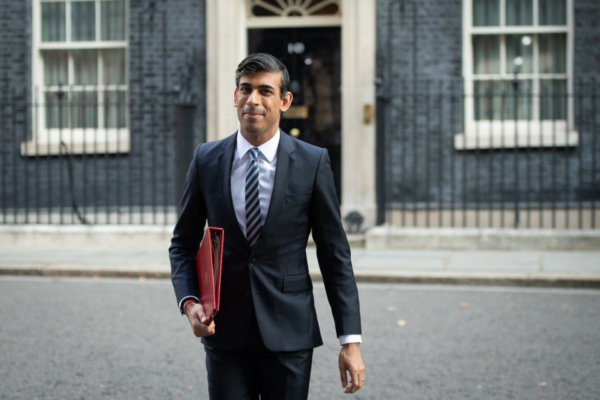 Rishi Sunak in a sharp black suit walking away from a goverment building
