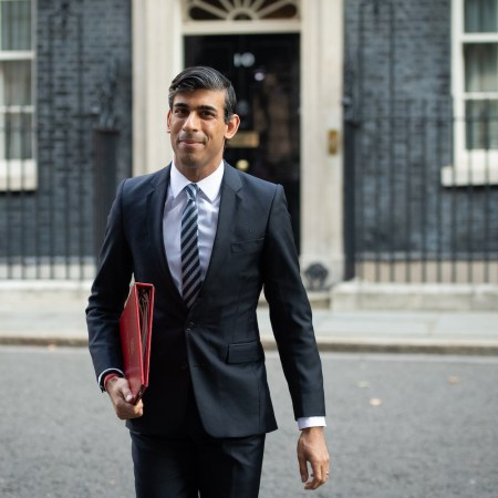 Rishi Sunak in a sharp black suit walking away from a goverment building