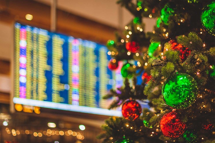 An airport with a decorated Christmas tree in the foreground and a flight departures display visible in the background