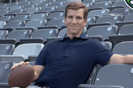 Eli Manning relaxing with a football in a stadium seat.