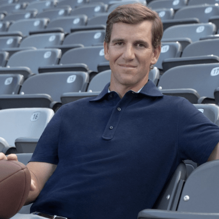 Eli Manning relaxing with a football in a stadium seat.