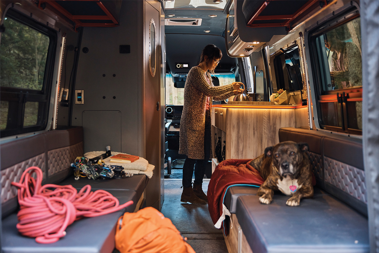The interior of the Airstream Interstate 24X, a Class B motorhome, with a dog sitting on a seat and a woman making coffee