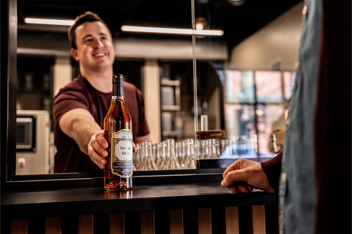An employee at Barrels and Billets hands over a bottle of custom bourbon to a customer